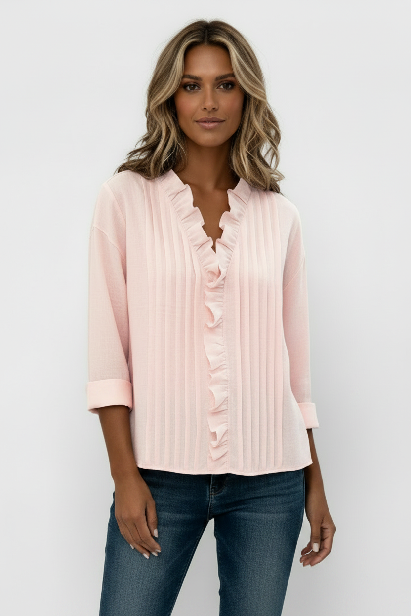 Person wearing a light pink blouse with ruffled details on a plain background