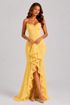 Woman wearing a yellow evening gown with ruffled details on a gray background