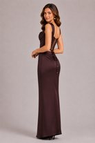 Woman wearing a burgundy evening gown with lace detailing on a plain background
