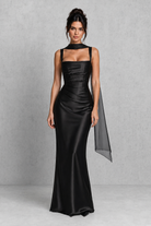 Woman wearing a black satin gown with a cape on a gray background