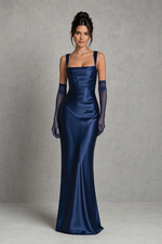 Woman wearing a navy blue evening gown with matching gloves against a gray background