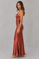 Woman wearing a rust-colored satin gown against a gray background