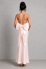 Pink evening gown with a large bow detail on the back, worn by a model against a gray background.