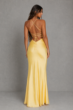 A woman modeling a floor-length yellow satin gown from the back, showing a strappy open back and flared skirt, against a gray studio backdrop.