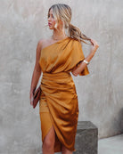 Woman wearing a mustard yellow one-shoulder dress against a plain background