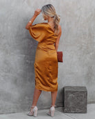 Woman in a mustard yellow dress standing against a gray wall.