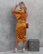 Woman in a mustard yellow dress standing against a gray wall.