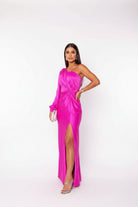 Woman in a bright pink one-shoulder dress standing in a modern interior setting.