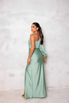 Woman in a light green evening gown standing against a white wall.