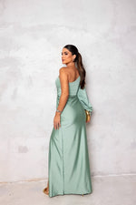 Woman in a light green evening gown standing against a white wall.