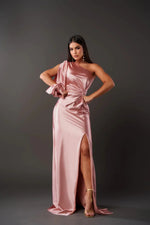 Woman wearing a pink satin one-shoulder dress with a slit on a gray background