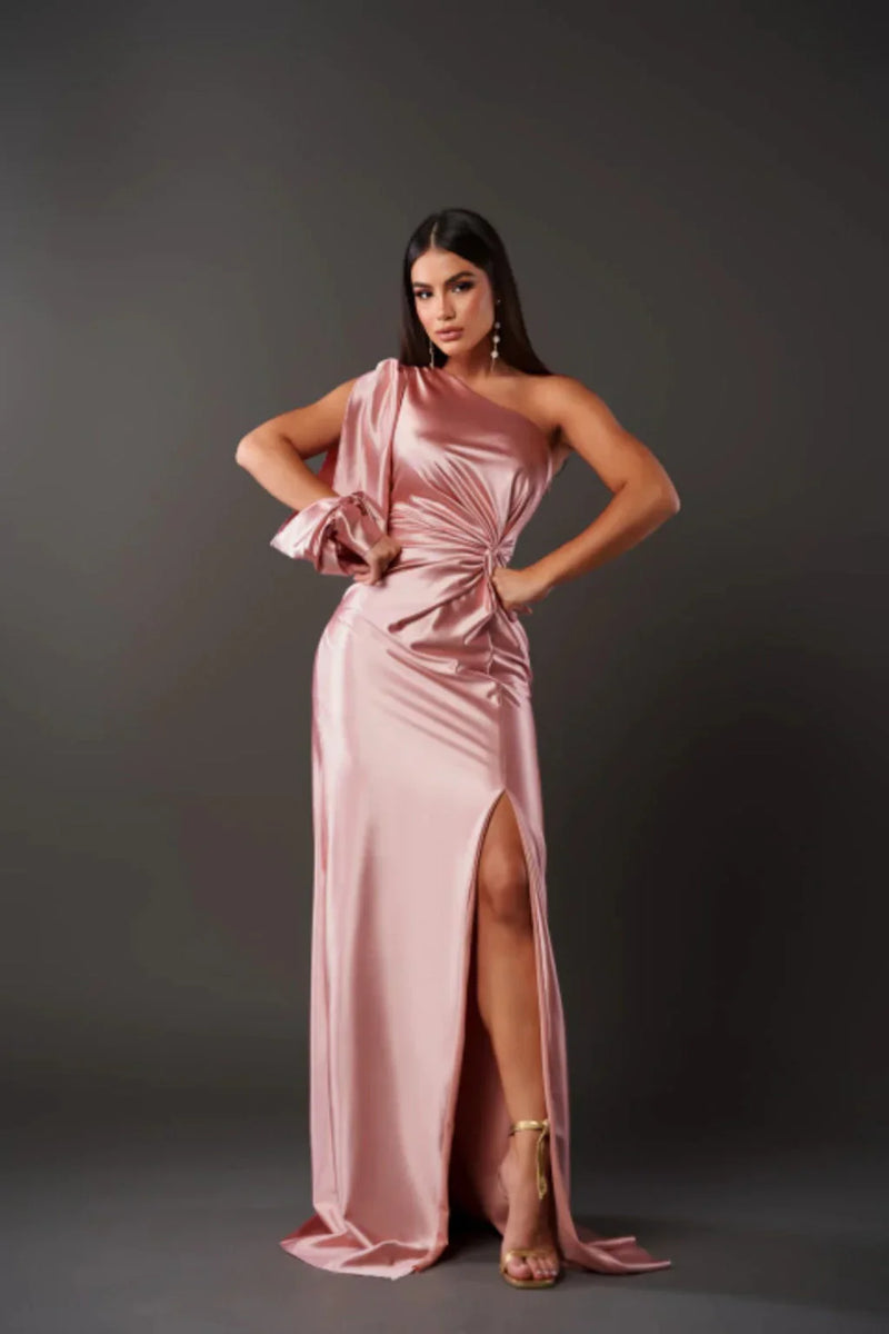 Woman wearing a pink satin one-shoulder dress with a slit on a gray background