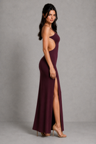 Woman wearing a burgundy evening gown with a high slit on a gray background