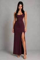 Woman wearing a burgundy evening gown with a high slit on a gray background
