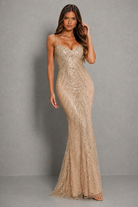 A woman modeling a floor-length champagne beige sequined gown with spaghetti straps and a sweetheart neckline, standing against a neutral gray studio backdrop.