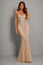 A woman modeling a floor-length champagne beige sequined gown with spaghetti straps and a sweetheart neckline, standing against a neutral gray studio backdrop.