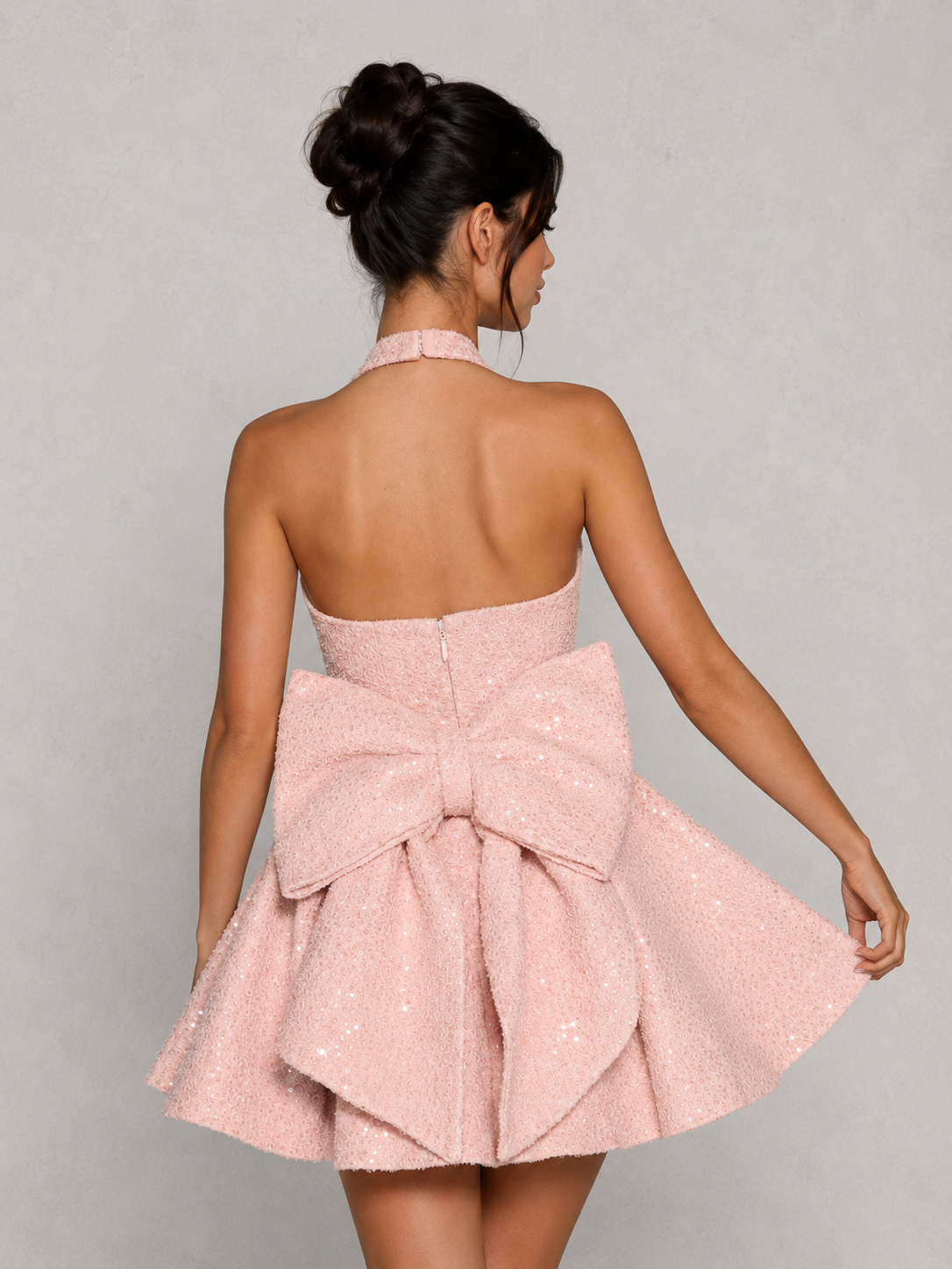 Woman wearing a pink dress with a large bow at the back against a gray background