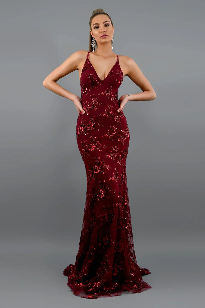 Woman wearing a burgundy sequin evening gown against a gray background