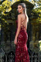 Woman in a red sequin dress standing in front of an ornate stone archway.