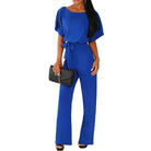 Woman wearing a blue jumpsuit holding a black clutch on a white background