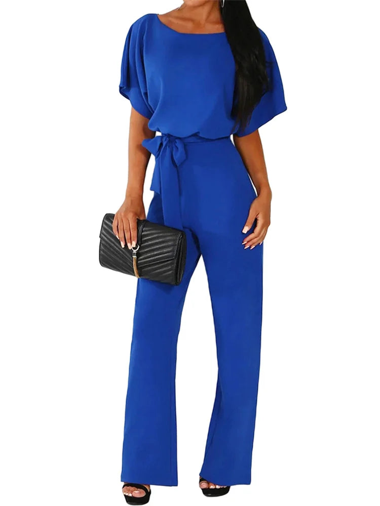 Woman wearing a blue jumpsuit holding a black clutch on a white background