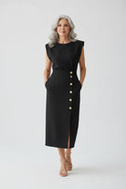 Woman wearing a black dress with buttons standing in a modern interior setting.