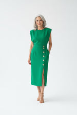 Woman wearing a green dress with buttons standing in a modern interior setting.