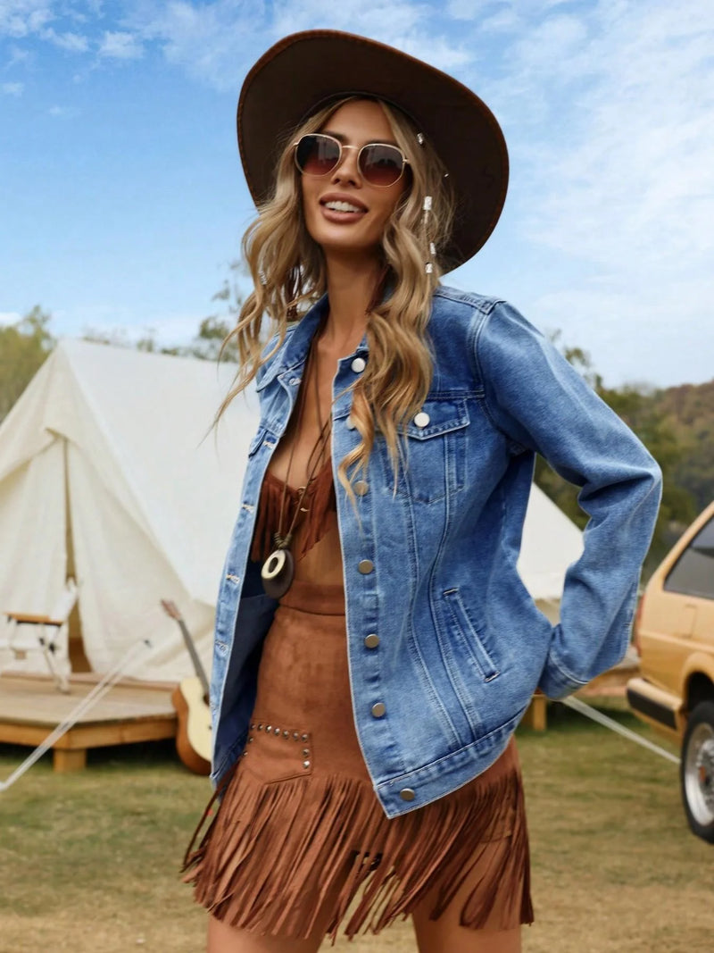 Woman in a denim jacket and brown fringed dress standing outdoors with tents and a car in the background.