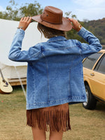 Person wearing a denim jacket and brown fringed skirt with a cowboy hat, standing outdoors.