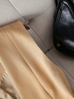 Beige pants on a light gray couch with a black bag beside them
