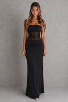 Woman wearing a black strapless gown with lace detailing against a gray background