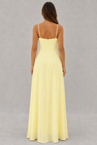 Woman wearing a light yellow dress with thin straps on a gray background