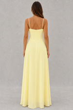 Woman wearing a light yellow dress with thin straps on a gray background