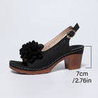 Black sandal with a wooden heel and floral detail on a light gray background