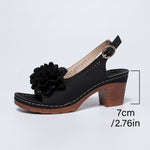 Black sandal with a wooden heel and floral detail on a light gray background