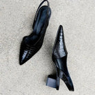 Black crocodile-patterned high-heeled shoes on a light gray surface