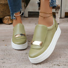 Green slip-on sneakers with gold accents worn by a person on a concrete floor.