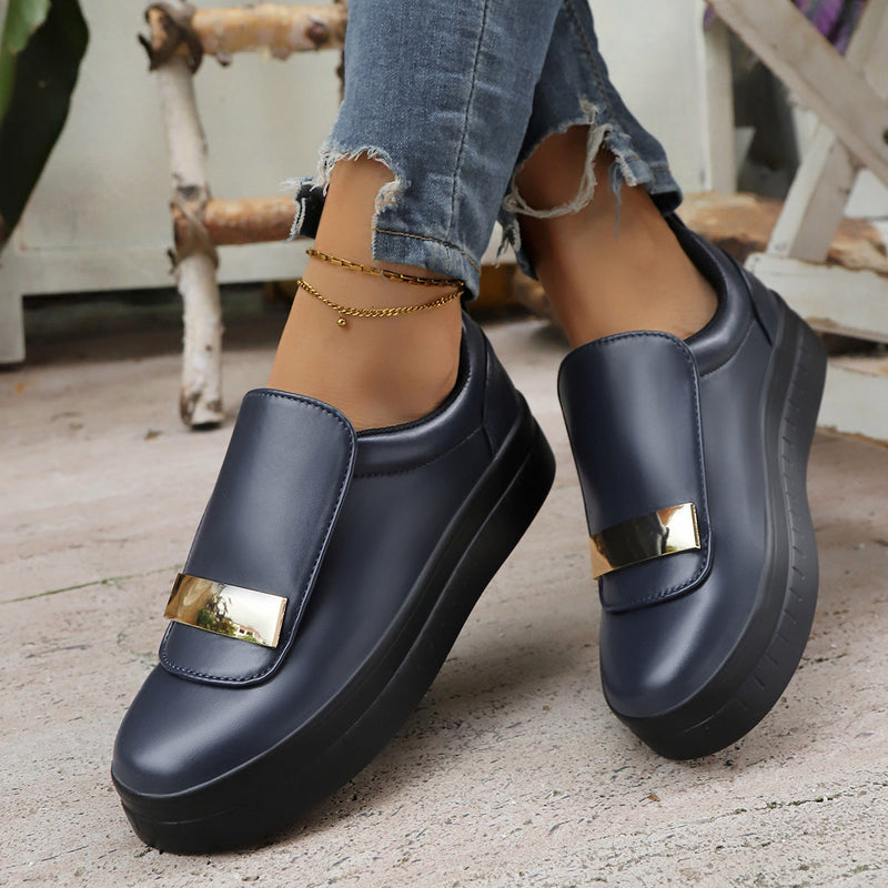 Navy slip-on shoes with gold accents worn indoors on a wooden floor.