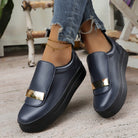 Navy slip-on shoes with gold accents worn indoors on a wooden floor.