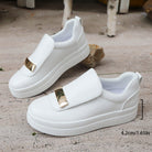 White slip-on shoes with gold accents on a concrete surface.
