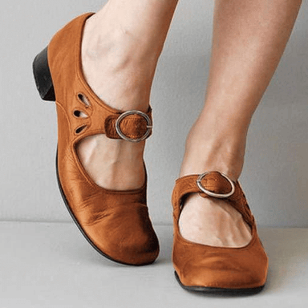 Brown shoes with buckles worn by a person on a gray background