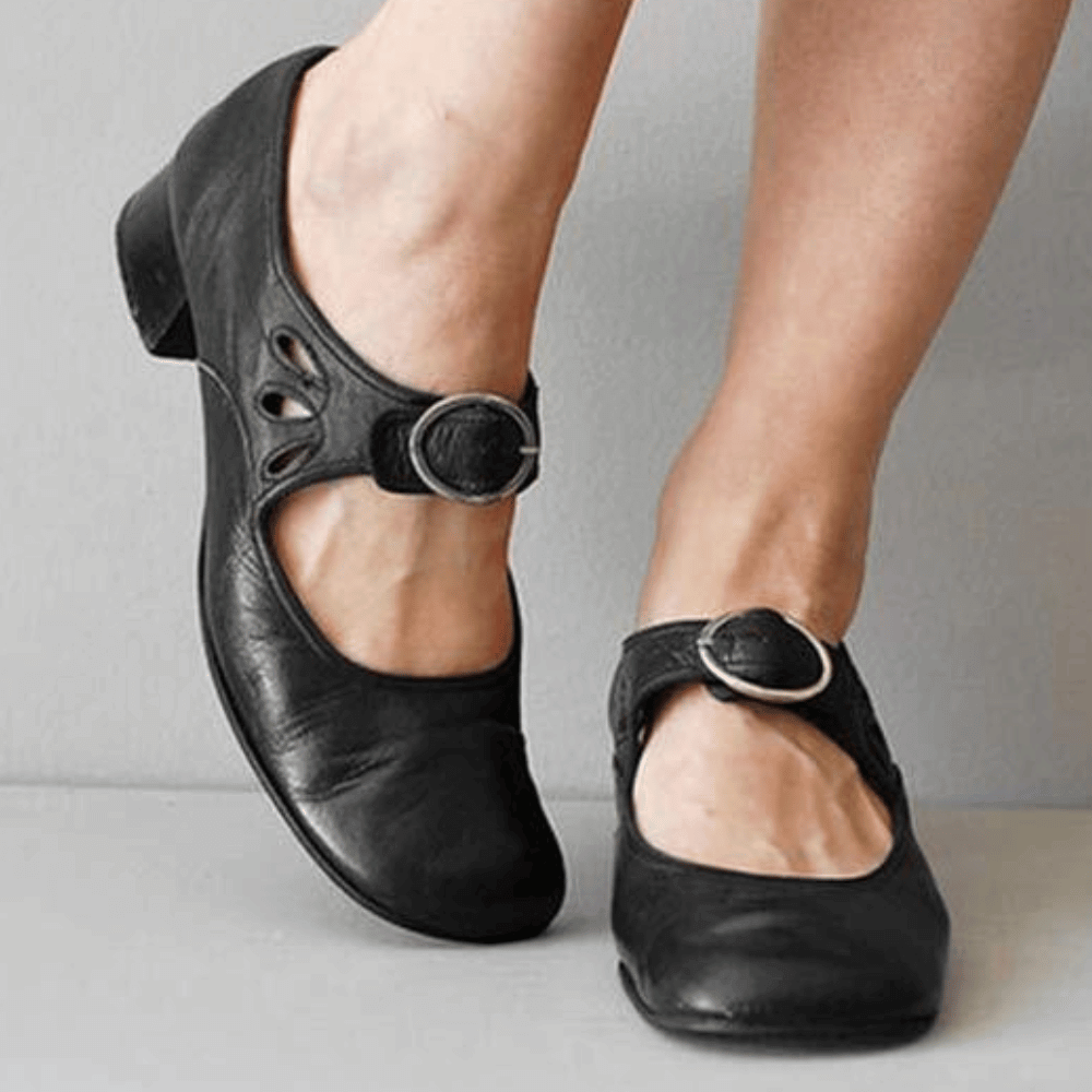 Black leather shoes with buckles worn by a person on a neutral background