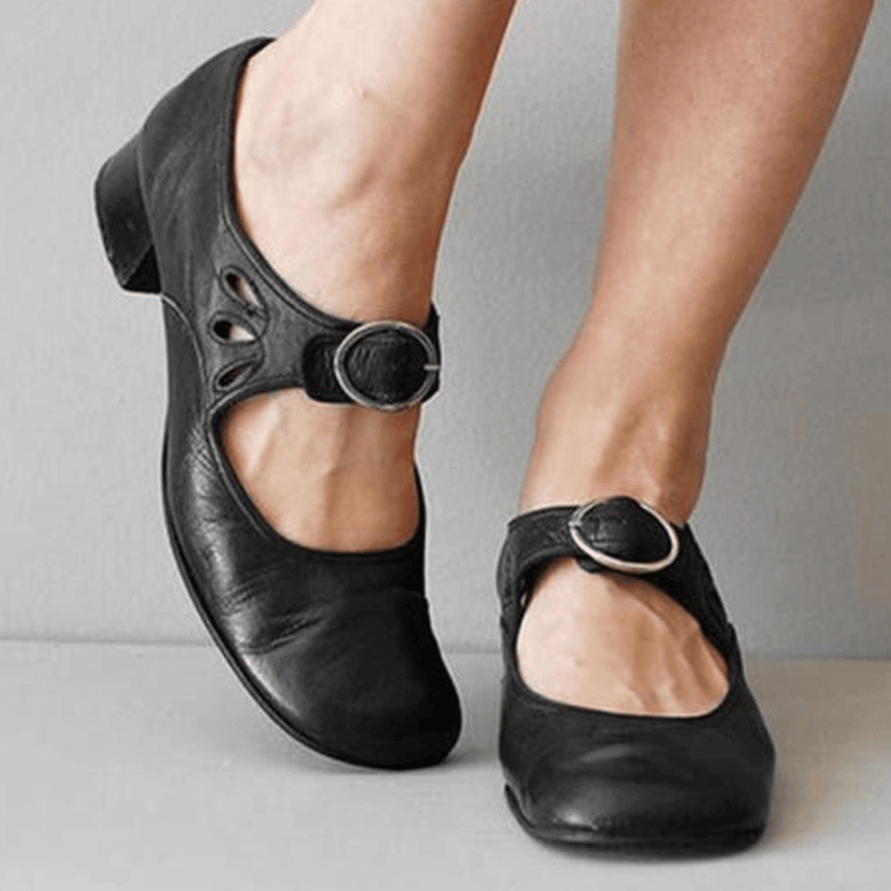 Black leather shoes with buckles worn by a person on a neutral background