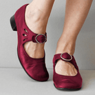 Maroon shoes with buckles worn by a person on a neutral background