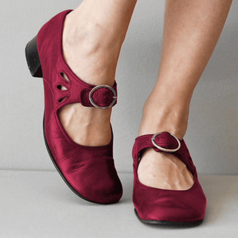 Maroon shoes with buckles worn by a person on a neutral background