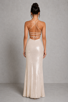 Woman wearing a long, light-colored dress with thin straps against a gray background