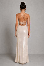 Woman wearing a long, light-colored dress with thin straps against a gray background