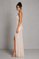 Woman wearing a long, elegant dress with a high slit on a plain background