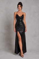 Woman wearing a black sequin dress with a high slit on a gray background