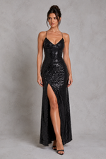 Woman wearing a black sequin dress with a high slit on a gray background